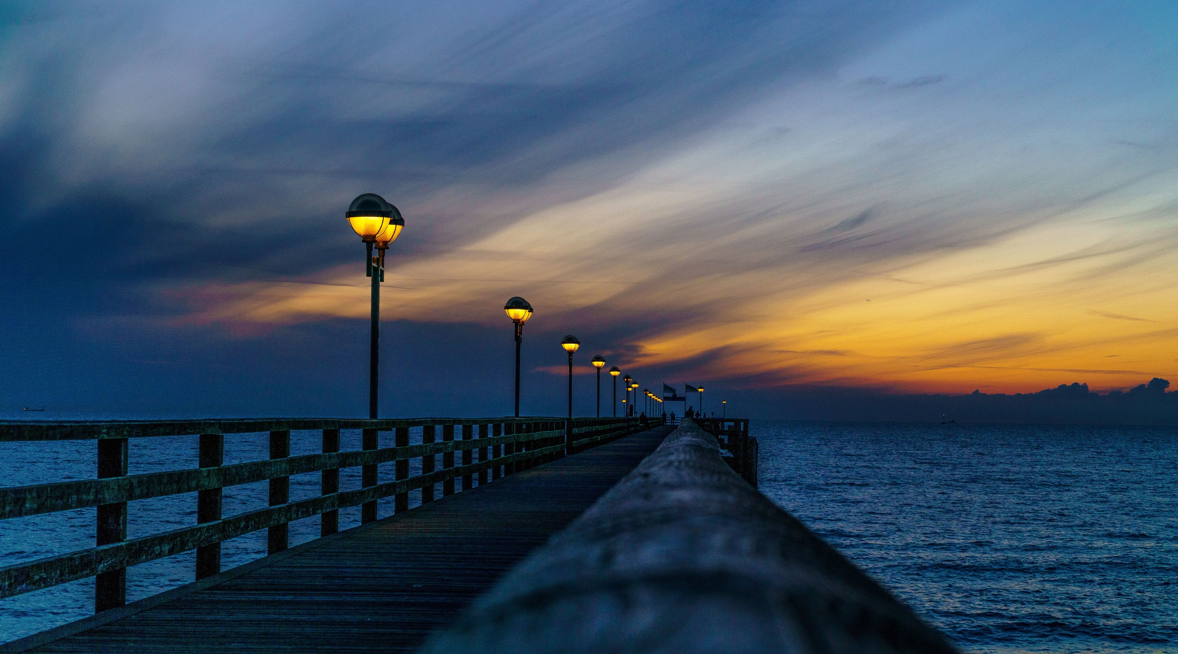 Langer Steg mit Laternen, der ins Meer führt, bei Sonnenuntergang mit buntem Himmel.